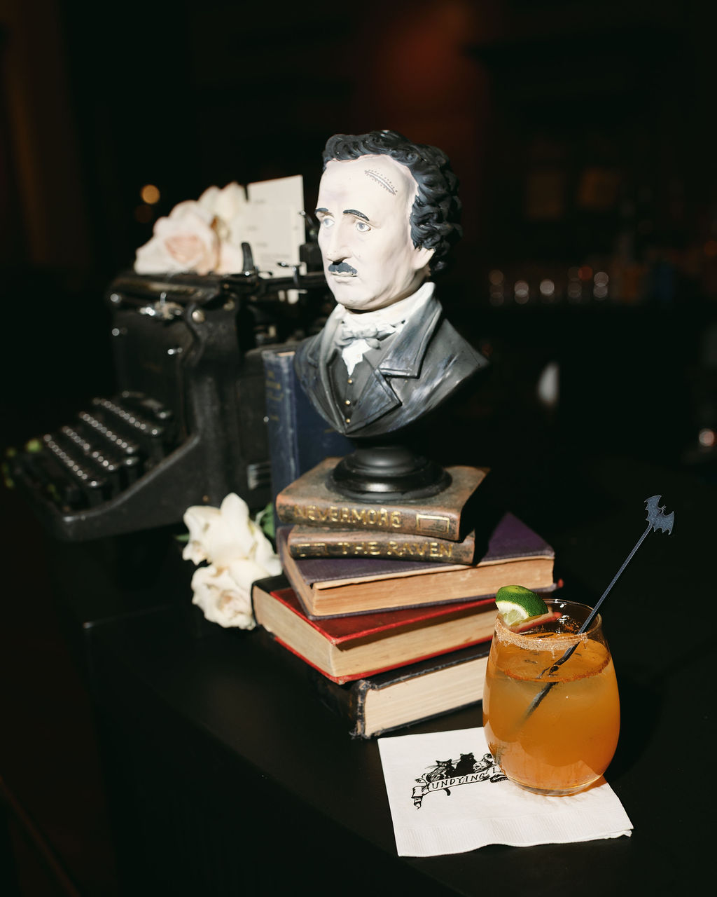 Madeline-Serio-Photography_Mollie-Sam_10-26-24 (53) Edgar Allen Poe bust on a black bar with a drink.